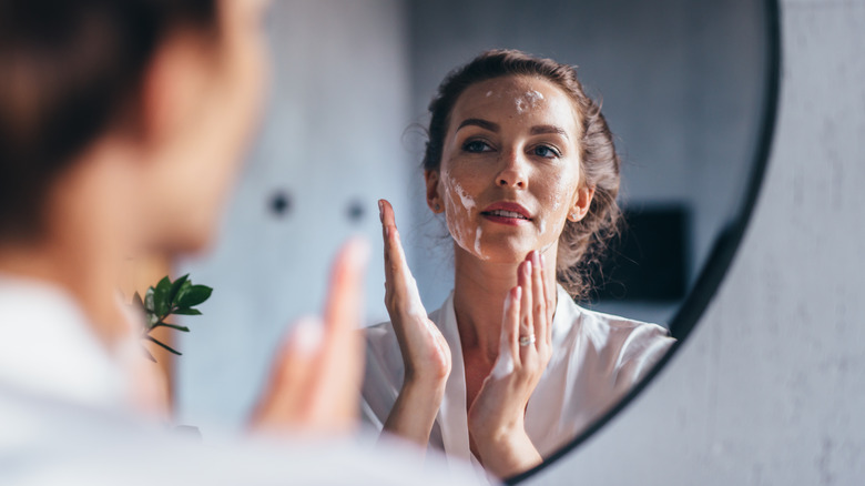 woman washing her face in front of a mirror