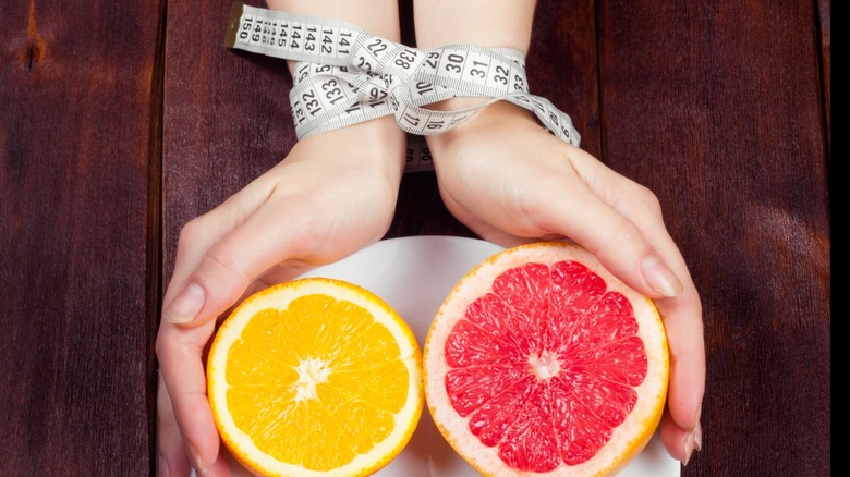 Hands wrapped in measuring tape holding grapefruit