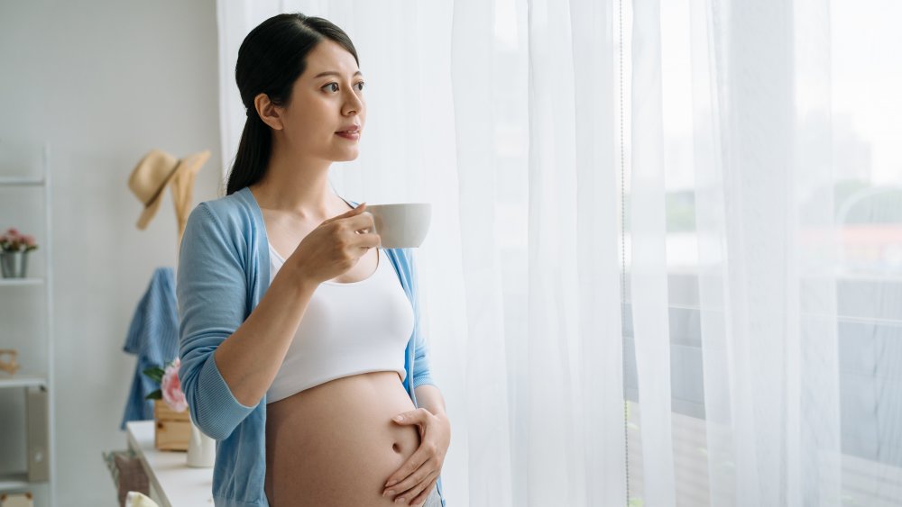Pregnant woman holding her baby bump and drinking tea