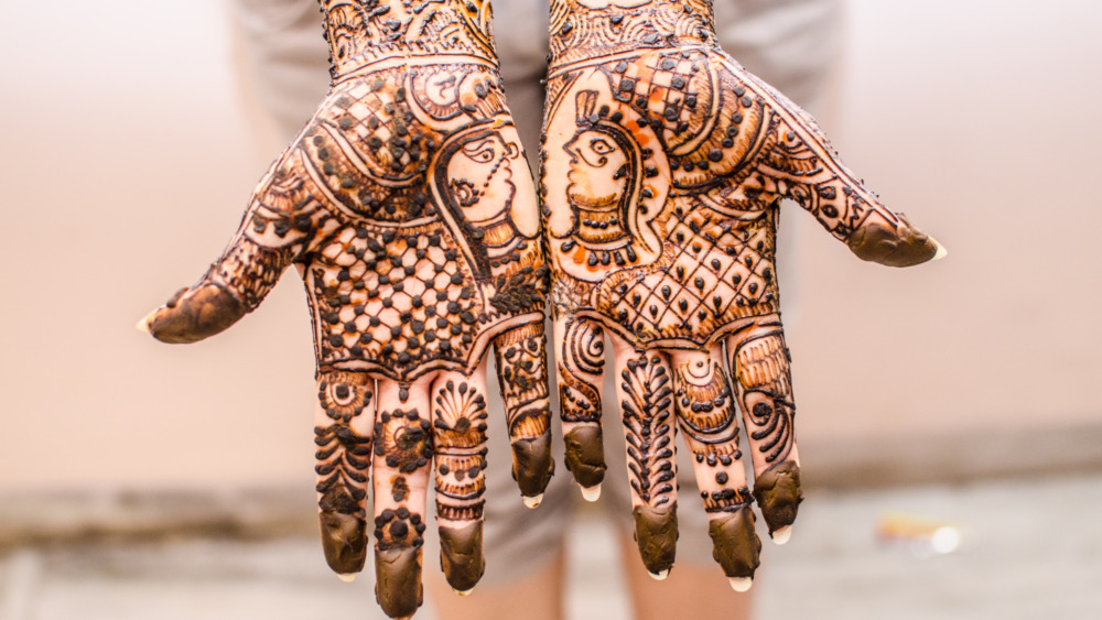 Two hands held palm out covered in an intricate design made with henna paste