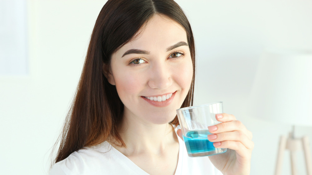 A smiling woman holding a glass of mouthwash 
