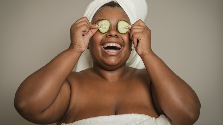 Woman smiles, puts cucumbers over her eyes 