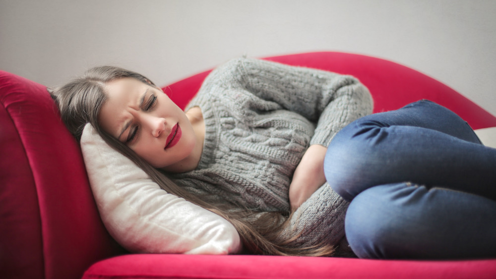 Woman on the couch clutching stomach in pain 