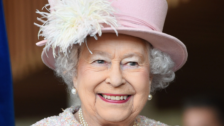 Queen Elizabeth smiling in a pink hat 