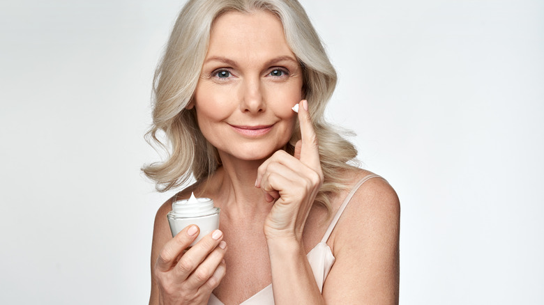 mature woman applying moisturizer to face