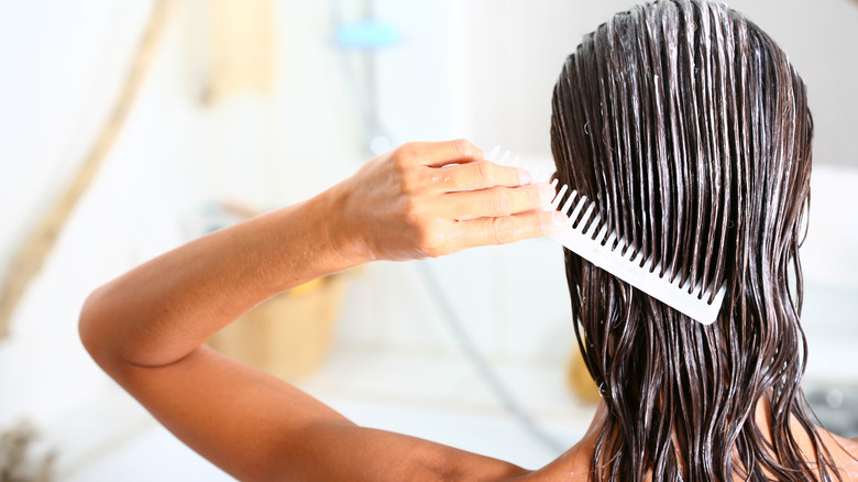 Woman brown hair applies conditioner to hair with comb