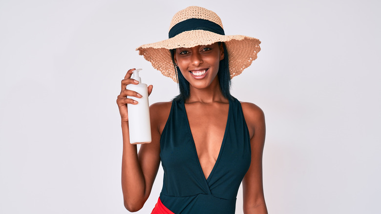 Woman in swimsuit holding bottle of sunscreen