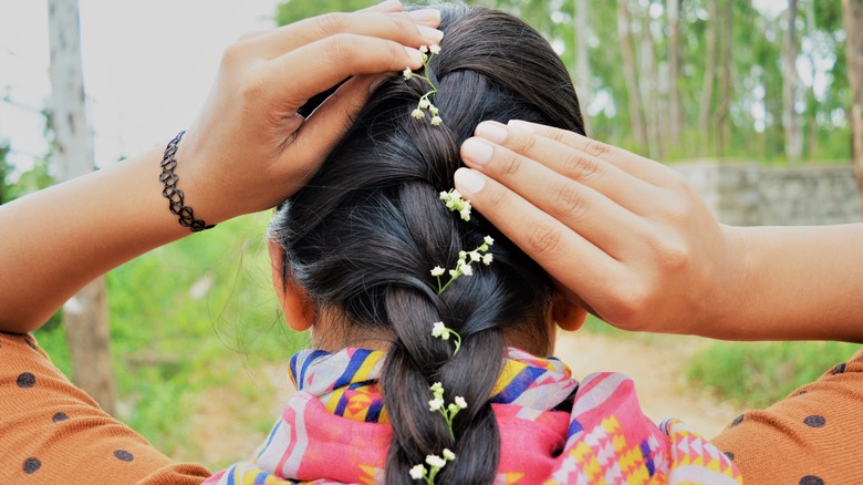 Brunette putting baby's breath flowers into her French braid.
