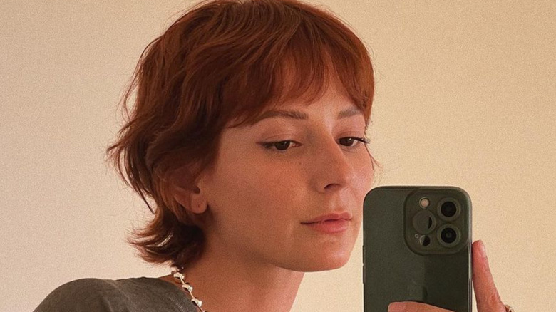 Redhead girl with short hair taking a mirror selfie with a green iPhone