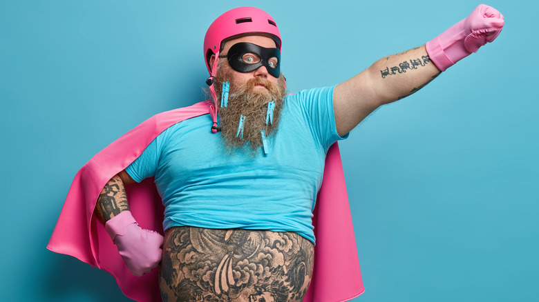 man wearing pink cape with tattoos on stomach and arms