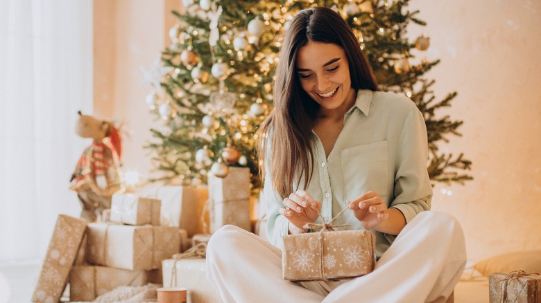 Woman smiling in front of a Christmas tree, holding a present