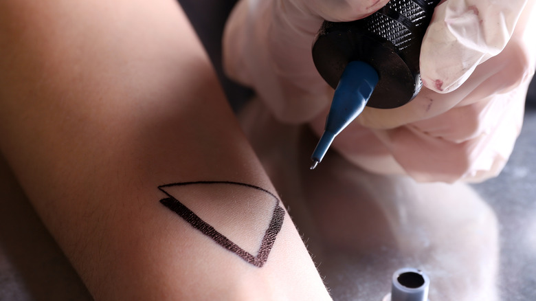 Tattoo artist tattooing triangle on arm