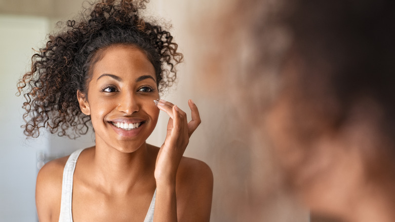 Woman smiling, putting lotion on her face