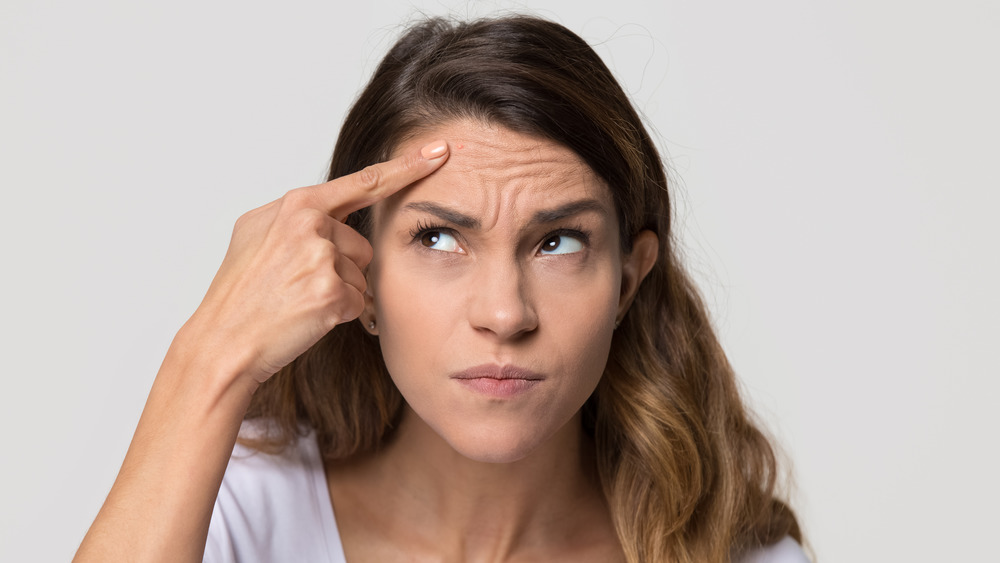 Woman looking annoyed and stress pointing at a pimple on her forehead