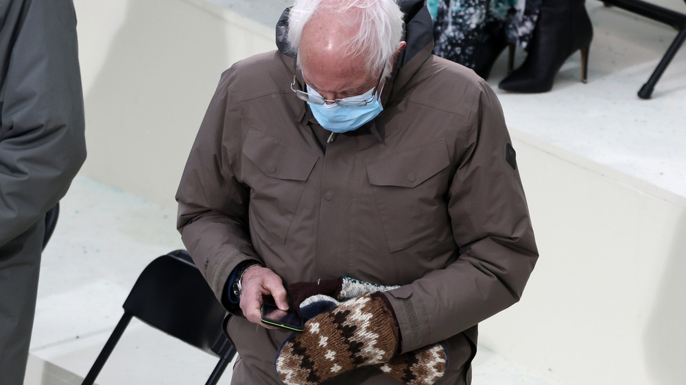 Bernie Sanders checking phone wearing mittens
