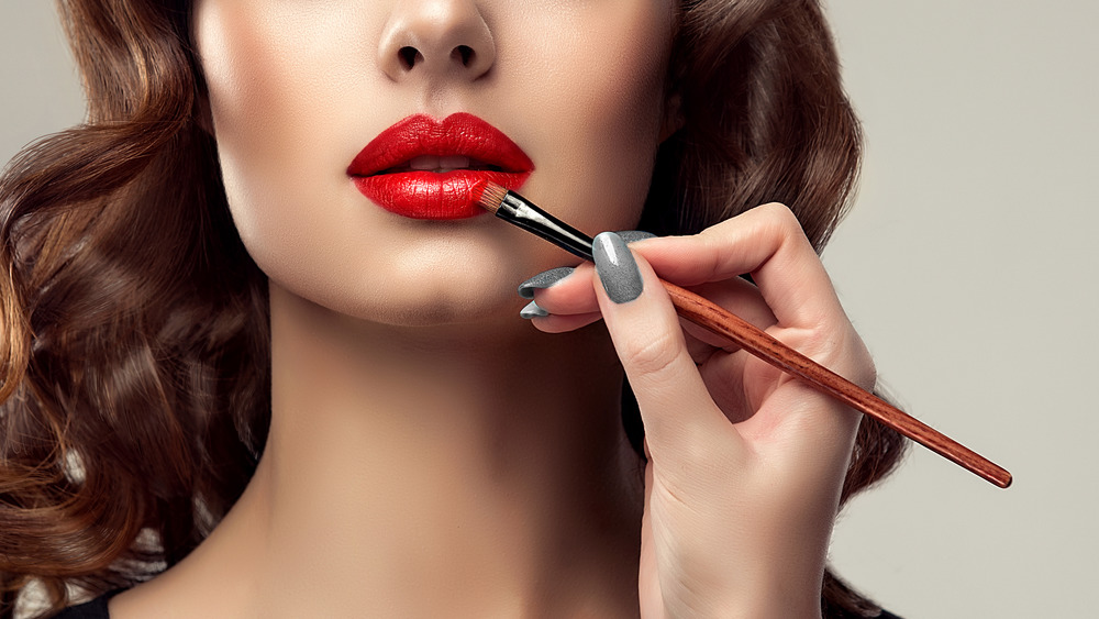 Woman uses brush to apply red lipstick