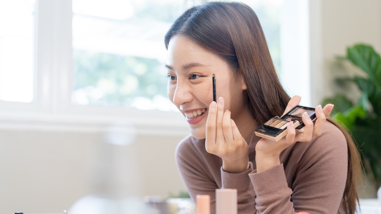 woman applying makeup and smiling