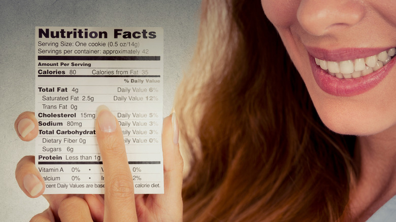 Smiling woman holding a nutrition facts label pointing to Trans Fat. 