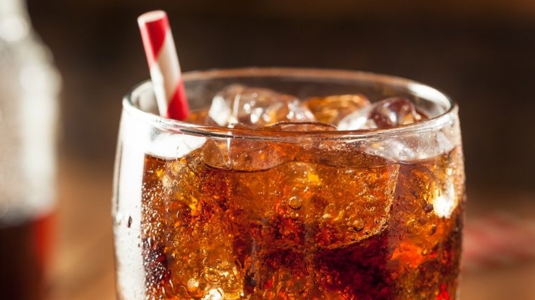 A glass of cola with ice and a straw
