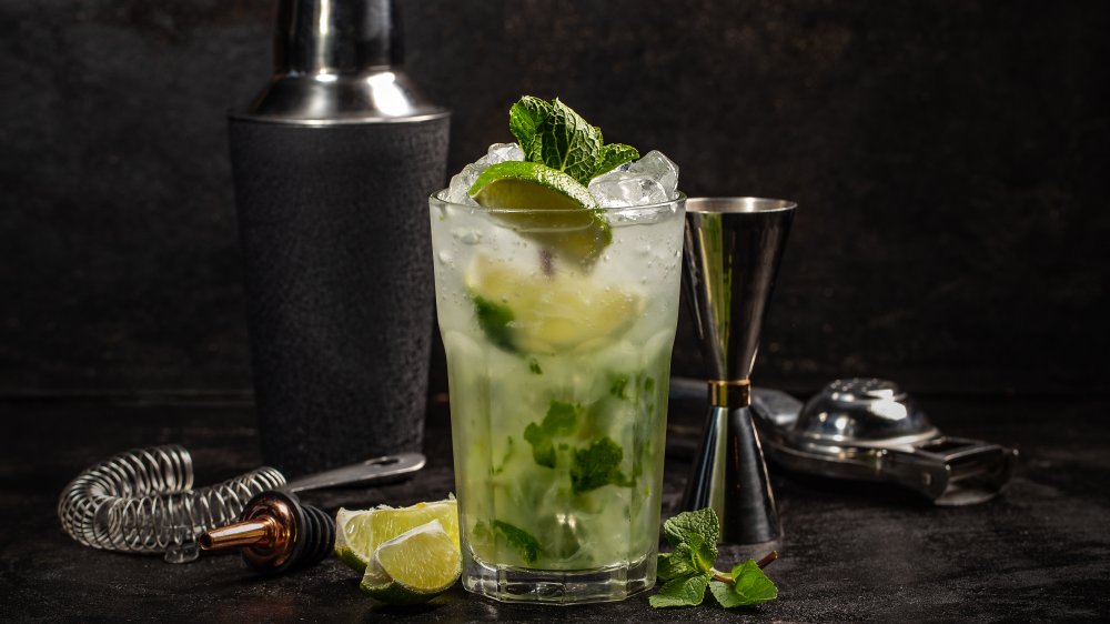 A mojito made with rum on a bar with ingredients and accessories