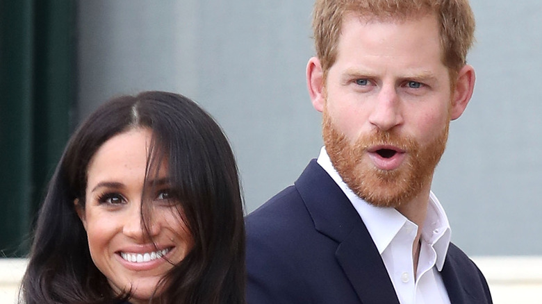 Meghan Markle smiling while Prince Harry looks shocked