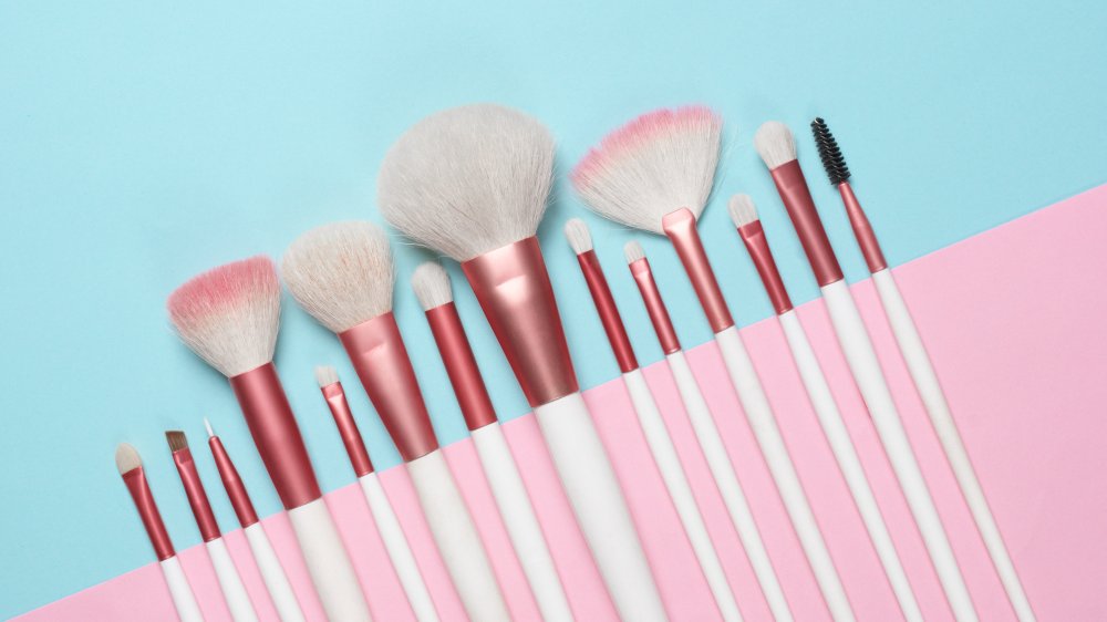 makeup brushes against a pale blue and pink background